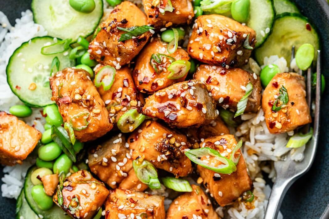 Close up view of a colorful Air Fryer Salmon rice bowl, filled with thinly sliced cucumbers, edamame beans, and sesame seeds.