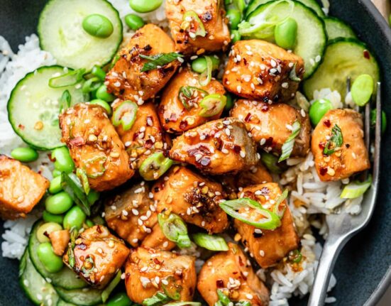Close up view of a colorful Air Fryer Salmon rice bowl, filled with thinly sliced cucumbers, edamame beans, and sesame seeds.