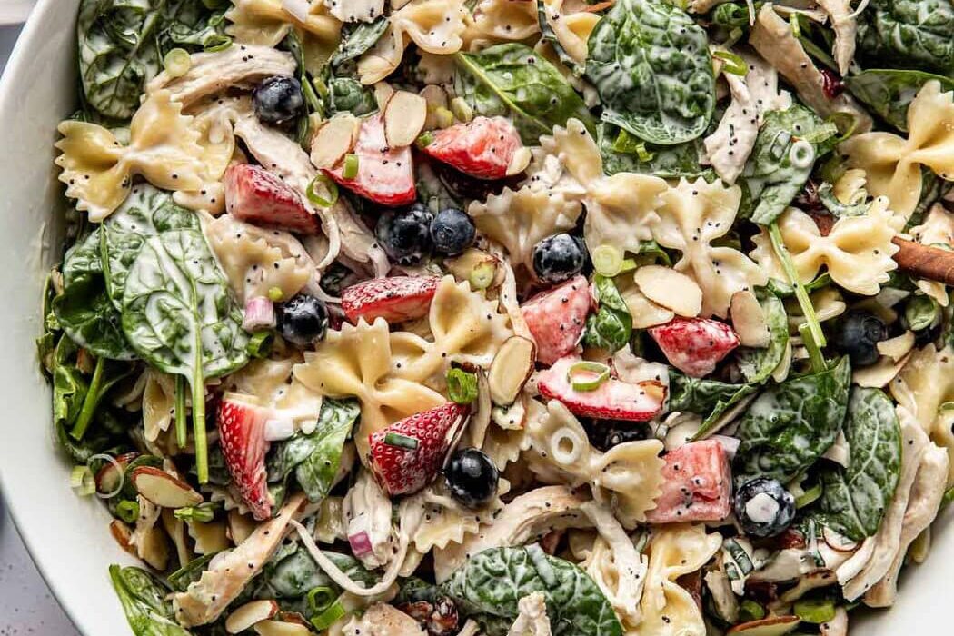 Overhead view of a large white bowl filled with Summer Berry Pasta Salad With Chicken and topped with sliced almonds and green onions.