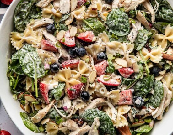 Overhead view of a large white bowl filled with Summer Berry Pasta Salad With Chicken and topped with sliced almonds and green onions.