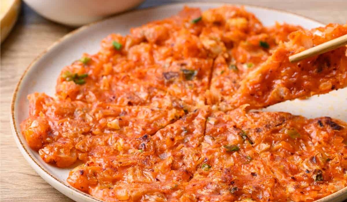 A Kimchi Pancake on a white plate being eaten with chopsticks
