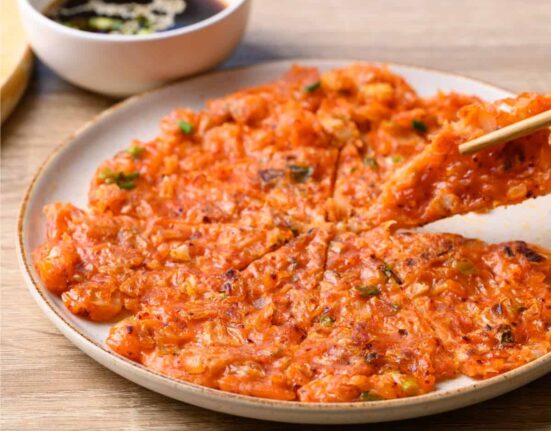 A Kimchi Pancake on a white plate being eaten with chopsticks