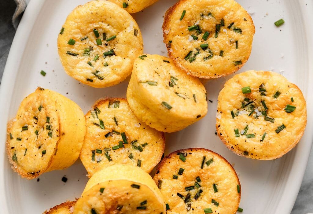 Close up view of a plate of egg bites topped with fresh chives and flakey sea salt.