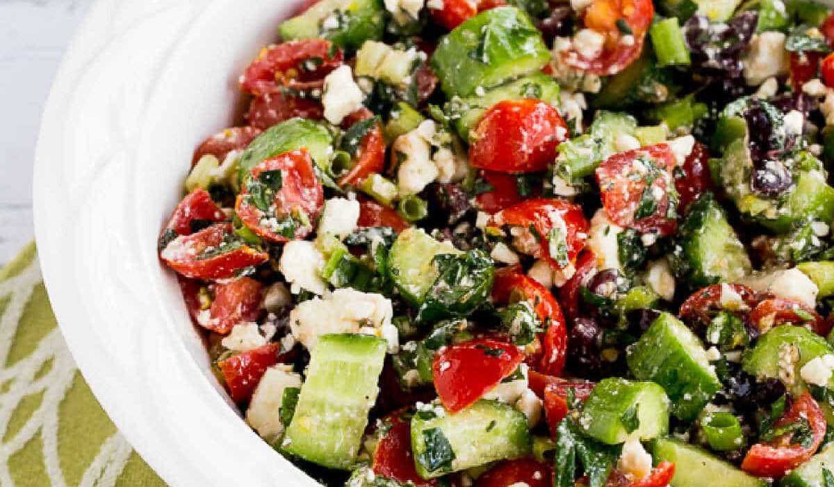 Square image of Tomato Cucumber Salad with Mint and Feta in white bowl on green-white-napkin.