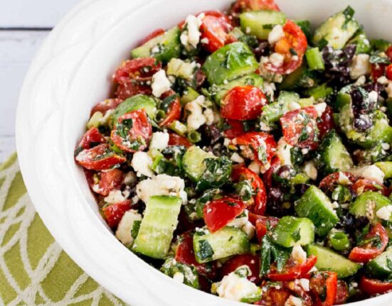 Square image of Tomato Cucumber Salad with Mint and Feta in white bowl on green-white-napkin.