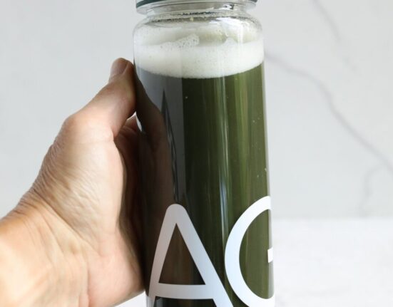Close up view of a hand holding a clear bottle of mixed AG1 greens showing the green color and foam on top.
