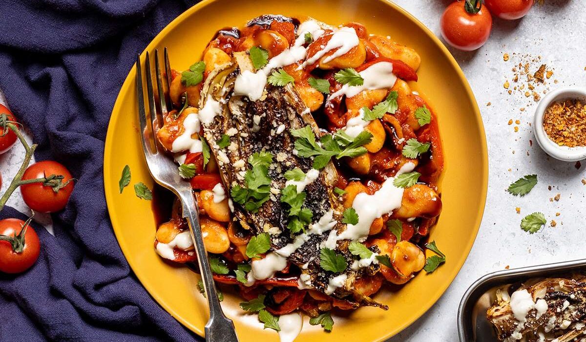 A yellow plate on the dinner table topped with butter beans in a spicy tomato sauce and seared cabbage on top.