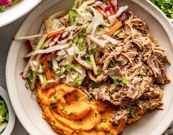 Overhead view of a white bowl filled with deep orange mashed sweet potatoes, pulled pork, and colorful fresh apple slaw.