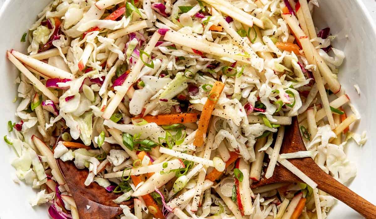 Overhead view of a white bowl filled with colorful Apple Slaw topped with black pepper and green onions.