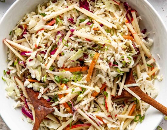Overhead view of a white bowl filled with colorful Apple Slaw topped with black pepper and green onions.