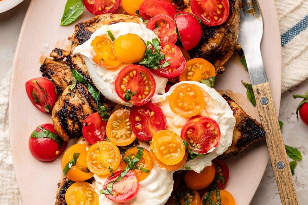 Overhead view of a platter filled with Grilled Chicken Caprese with Burrata topped with fresh basil.