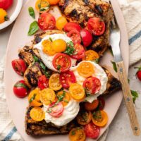 Overhead view of a platter filled with Grilled Chicken Caprese with Burrata topped with fresh basil.