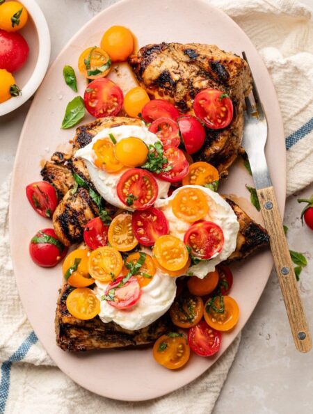Overhead view of a platter filled with Grilled Chicken Caprese with Burrata topped with fresh basil.