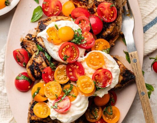 Overhead view of a platter filled with Grilled Chicken Caprese with Burrata topped with fresh basil.