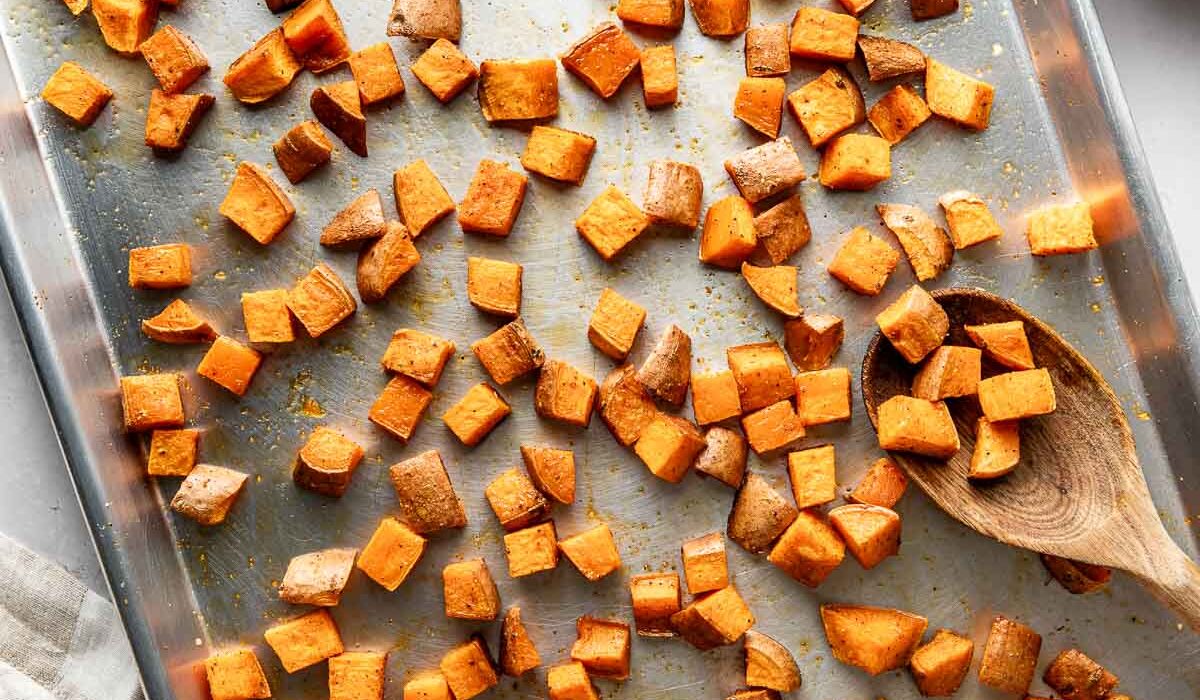 Overhead view of a metal sheet pan filled with freshly Roasted Sweet Potatoes topped with seasonings and crisp on the edges.