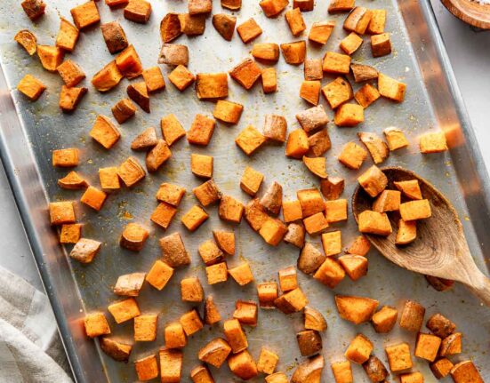 Overhead view of a metal sheet pan filled with freshly Roasted Sweet Potatoes topped with seasonings and crisp on the edges.