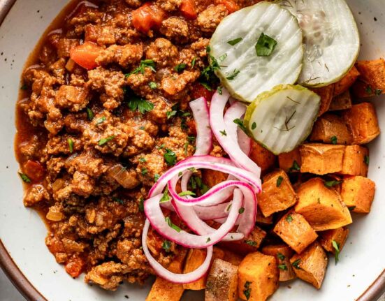 Overhead view of a bowl of sloppy joe meat, roasted sweet potatoes, pickled red onions, and crisp pickle chips.