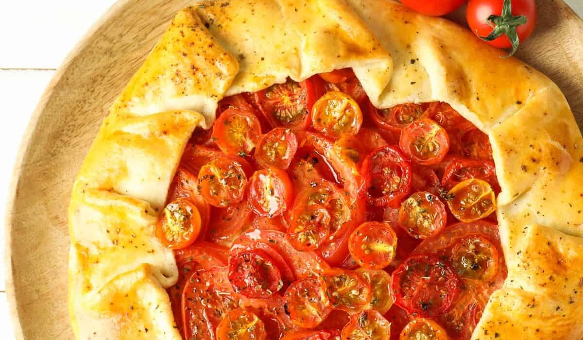 A Tomato Galette on a neutral surface with fresh tomatoes next to it
