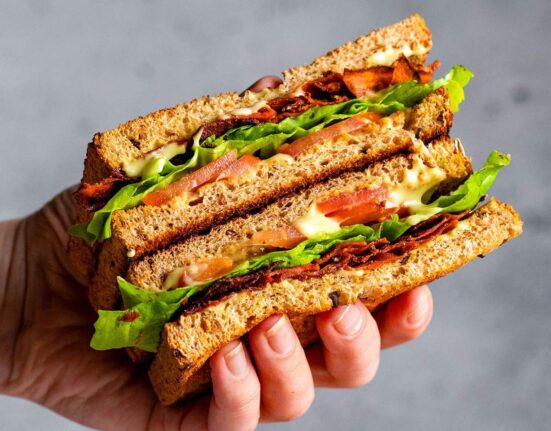A hand holding a vegan BLT sandwich with carrot bacon.