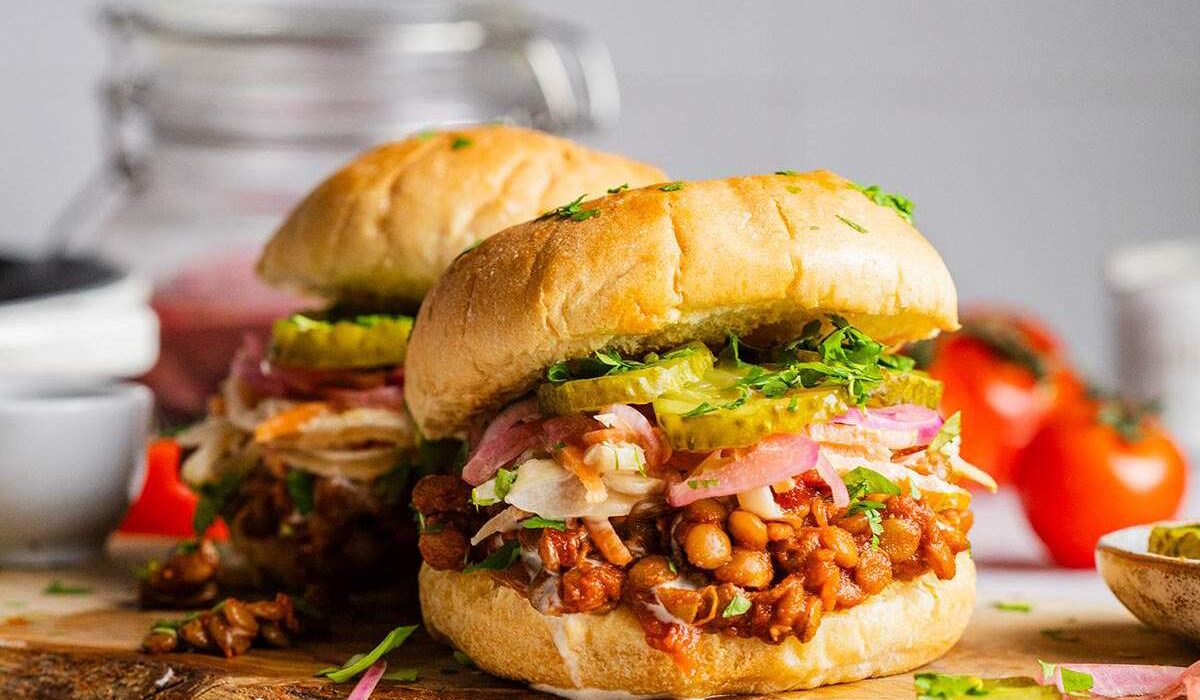 Two Vegan sloppy joes on a serving board with lentils and pickles.