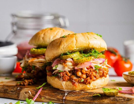 Two Vegan sloppy joes on a serving board with lentils and pickles.