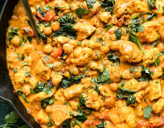 Overhead view cast iron skillet filled with chicken curry with chickpeas, cauliflower and spinach.