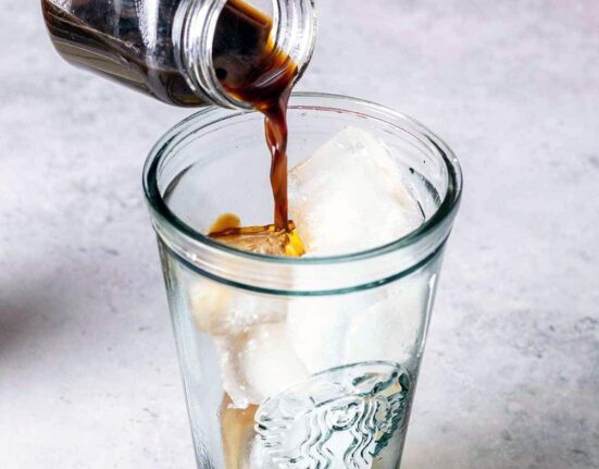 Pouring coffee into a tall glass with ice.