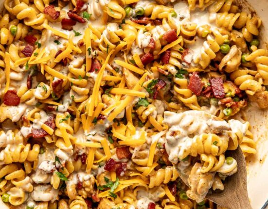 Overhead view of a skillet filled with One-Pot Chicken Bacon Ranch Pasta topped with crisp bacon pieces and shredded cheddar cheese.