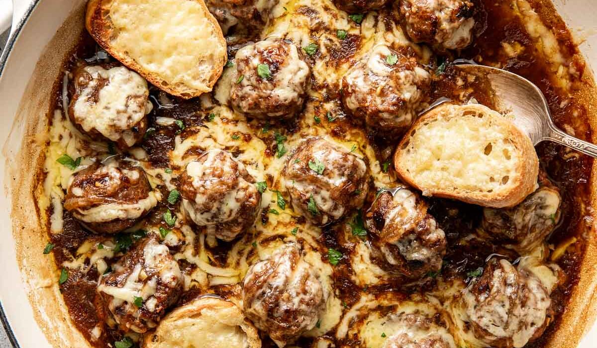 Overhead view of a skillet filled with French onion meatballs topped with cheese.