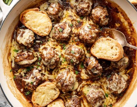Overhead view of a skillet filled with French onion meatballs topped with cheese.