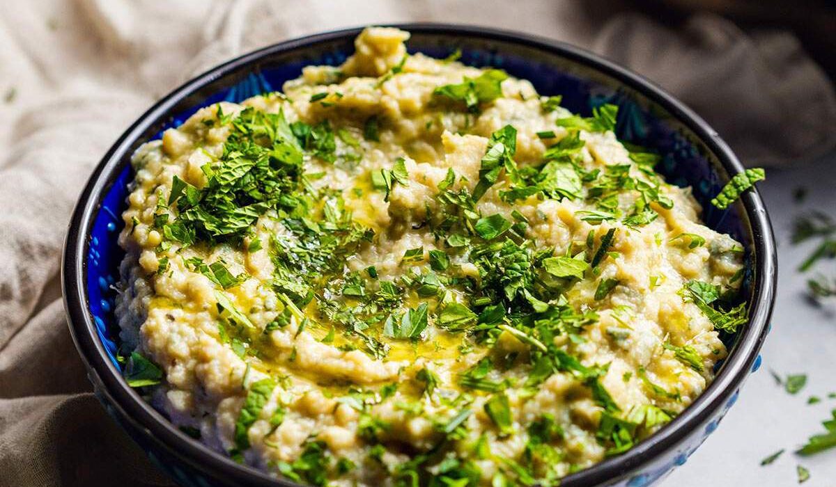A bowl filled with herb butter bean mash with fresh herbs on top.