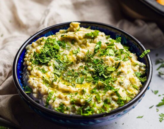 A bowl filled with herb butter bean mash with fresh herbs on top.