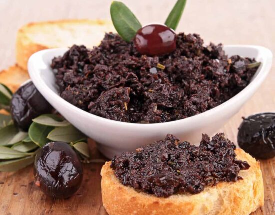 Olive Tapenade in a white bowl and spread on a piece of bread