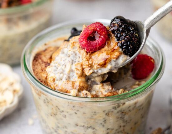 Close up view of a glass jar filled with Protein Overnight Oats topped with fresh berries and honey.