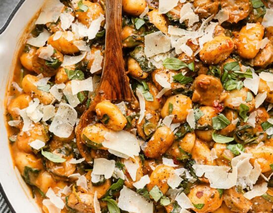 Overhead view of a skillet filled with gnocchi and sausage in a tomato sauce topped with shaved parmesan cheese.