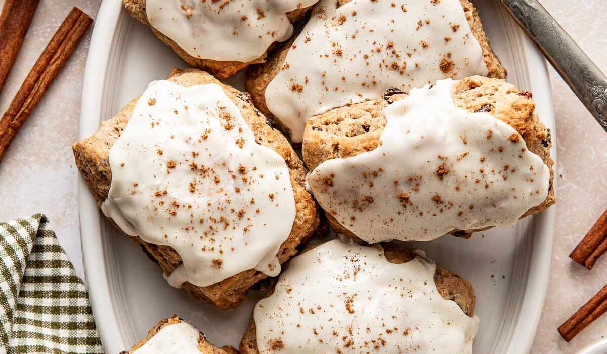 Overhead view of a white oblong platter filled with Cinnamon Raisin Biscuits topped with icing and sprinkled with cinnamon.