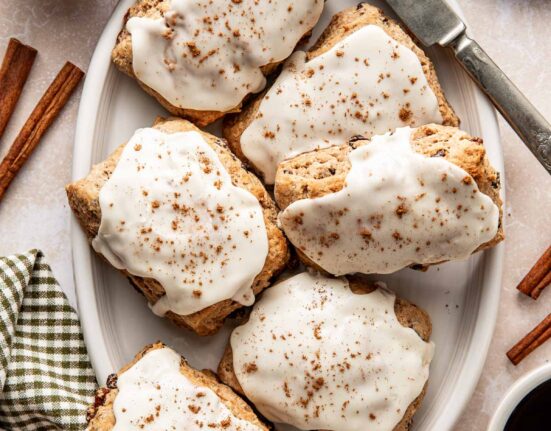 Overhead view of a white oblong platter filled with Cinnamon Raisin Biscuits topped with icing and sprinkled with cinnamon.