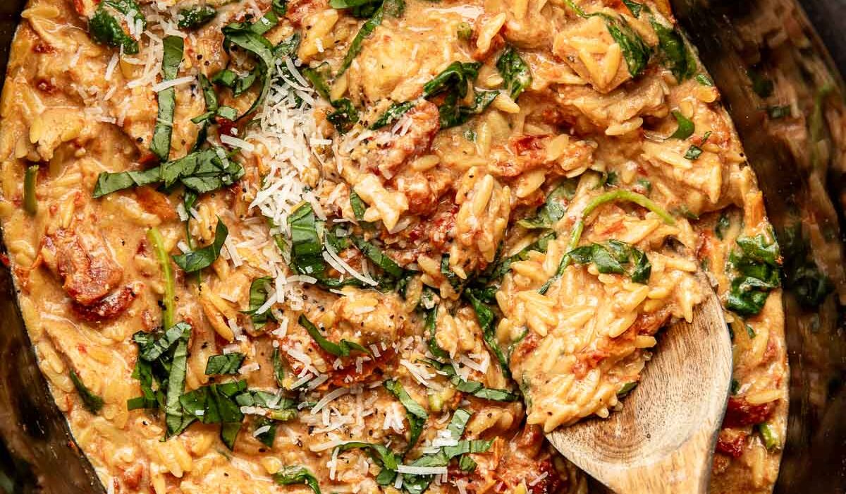 Overhead view of a slow cooker filled with Tuscan Chicken with Orzo and topped with fresh basil and shredded parmesan cheese.