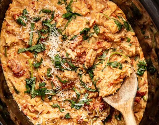 Overhead view of a slow cooker filled with Tuscan Chicken with Orzo and topped with fresh basil and shredded parmesan cheese.