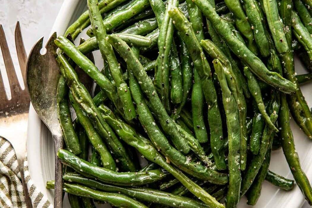 Close up view of a platter filled with freshly roasted green beans topped with salt and pepper.