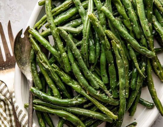 Close up view of a platter filled with freshly roasted green beans topped with salt and pepper.