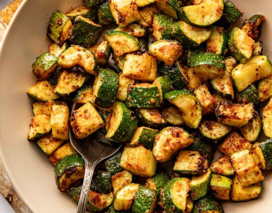 Overhead view of a ceramic bowl filled with Air Fryer Zucchini pieces with crisp texture.