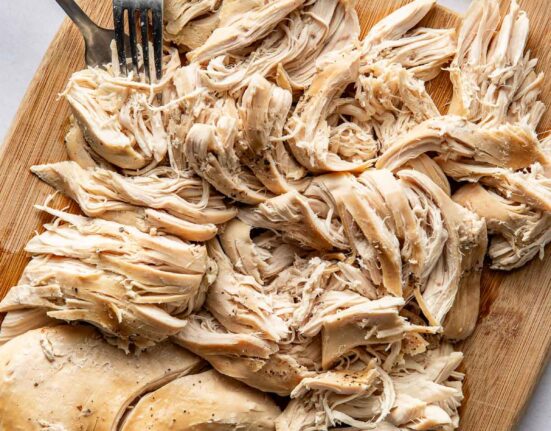 Overhead view of a wooden cutting board filled with shredded chicken and two forks.