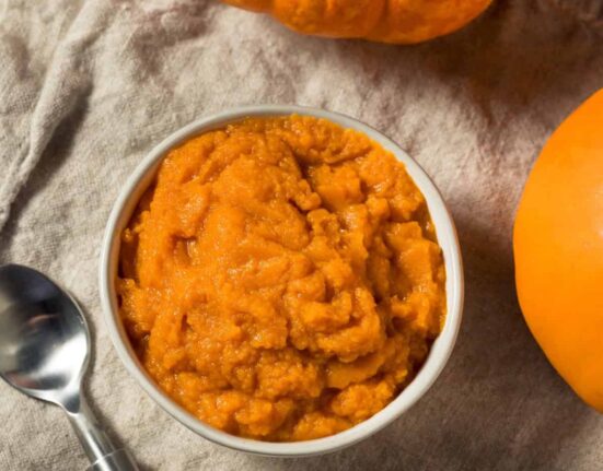 Overhead image of Pumpkin Puree in a white bowl next to pumpkins