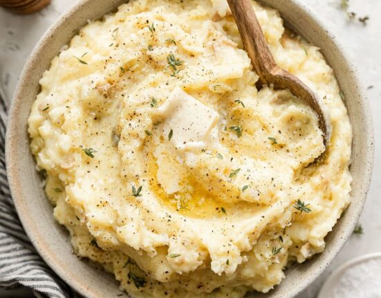 Close up view of a white ceramic bowl of freshly mashed potatoes topped with fresh herbs and melted butter.