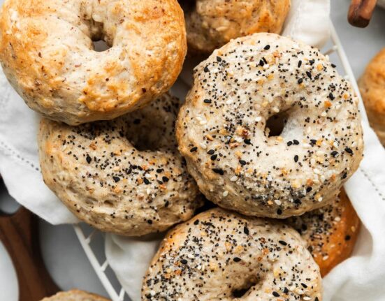 Freshly baked Greek yogurt bagels in a wire basket. Some of the bagels are top with Everything Bagel Seasoning.