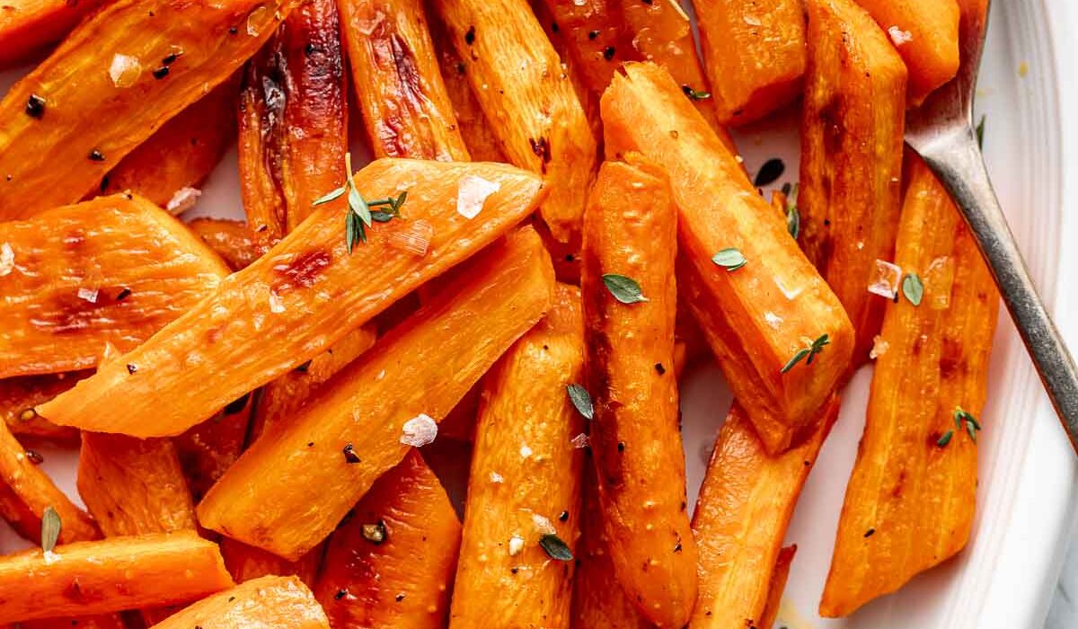 Close up view of freshly roasted carrots on a white platter showing flakey sea salt and fresh herbs on top.