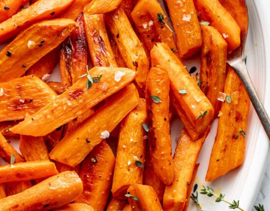 Close up view of freshly roasted carrots on a white platter showing flakey sea salt and fresh herbs on top.