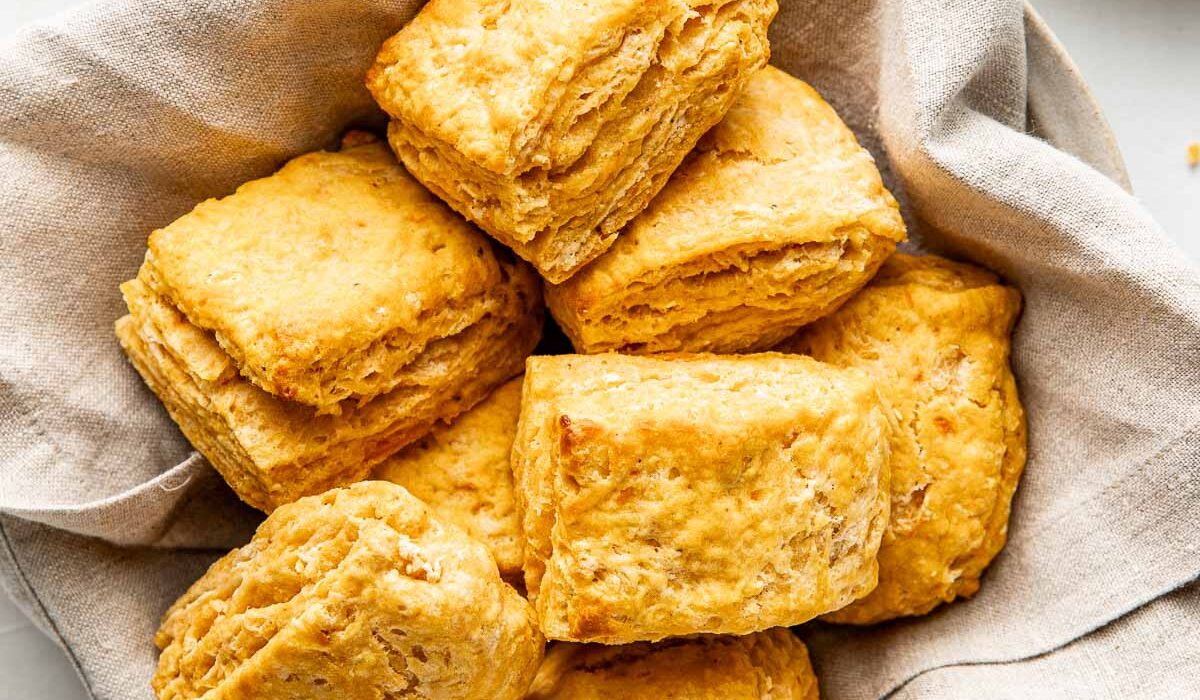 A bowl lined with a light colored linen napkin and filled with jewel-toned sweet potato biscuits.