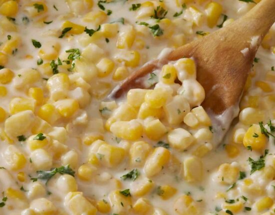 Overhead image of creamed corn in a skillet with a wooden spoon serving it